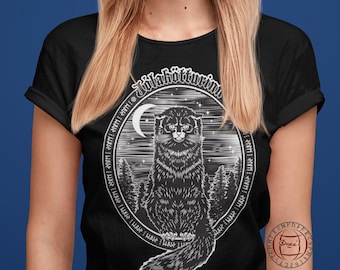 May include: A black t-shirt with a white graphic of a black cat sitting in a forest with a crescent moon and stars. The text "Jölakötturinn" is written in a circle around the cat.