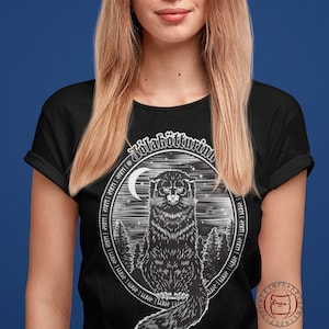May include: A black t-shirt with a white graphic of a black cat sitting in a forest with a crescent moon and stars. The text "J&ouml;lak&ouml;tturinn" is written in a circle around the cat.