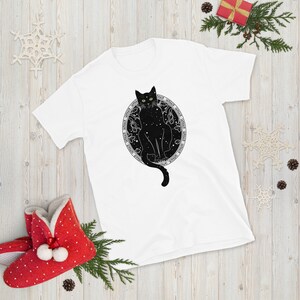May include: White t-shirt with a black cat sitting inside a circle of stars. The cat has green eyes and the text around the circle reads "Don't Tell Anyone, But I'm A Wizard".