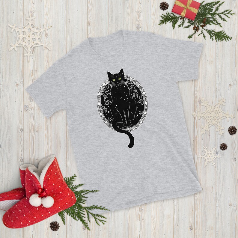 May include: A gray t-shirt with a black cat sitting inside a circle of stars. The cat has green eyes and a long tail. The text around the cat reads "Dark, Tender, Loyal, Fierce, Independent, Magical, Mysterious, Wild, Free".
