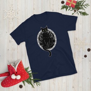 May include: A navy blue t-shirt with a black cat sitting inside a circle of stars. The cat has green eyes and the circle is surrounded by text.