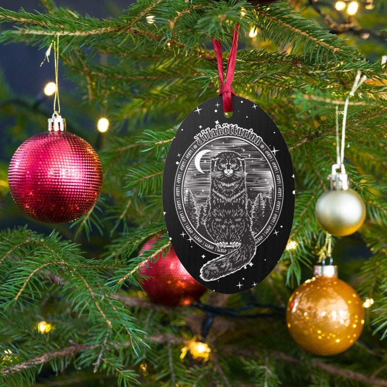 May include: Black and white Christmas ornament with a cat illustration and the text "Julekattens Jul" on a black background. The ornament is hanging on a Christmas tree.