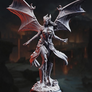 May include: A detailed, gray sculpture of a winged female figure with horns and outstretched arms. The figure is standing on a rocky base, with large, textured wings. The sculpture has a fantasy theme.
