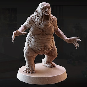 May include: A detailed, beige-colored miniature figure of a grotesque monster with an open mouth, sharp claws, and a round base. The figure has a wrinkled, textured appearance, with visible muscle definition and bulbous features.