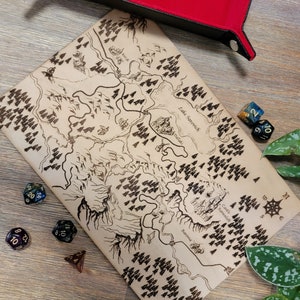 May include: A wooden map with a hand-drawn design of a fantasy landscape. The map features a lake, a castle, and a windmill. The map is surrounded by dice and a red felt dice tray.