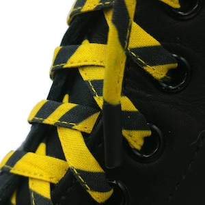 Peut inclure: Gros plan sur des bottes en cuir noir avec des lacets rayés jaunes et noirs. Les lacets sont noués en croisillon.