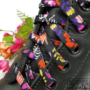 May include: Black shoelaces with a colourful floral and skeleton print. The shoelaces are tied on a black leather boot. The shoelaces are from the company "Super Laces".
