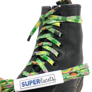 Può includere: Lacci verdi, gialli e rosa con un motivo arcobaleno e folletto. I lacci sono legati a uno stivale nero. I lacci hanno il testo "SUPERlacets" su un'etichetta bianca.
