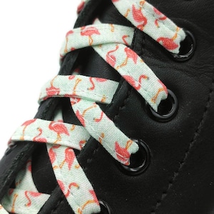 May include: Close-up of black shoelaces with a flamingo print on a white background. The shoelaces are tied in a criss-cross pattern on a black leather shoe.