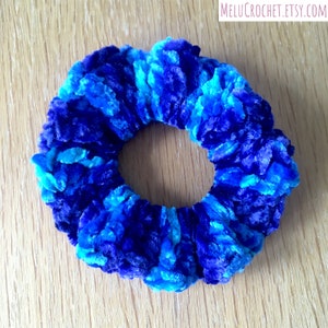 May include: A blue and turquoise fuzzy scrunchie hair tie. The scrunchie is made of a soft, plush fabric.