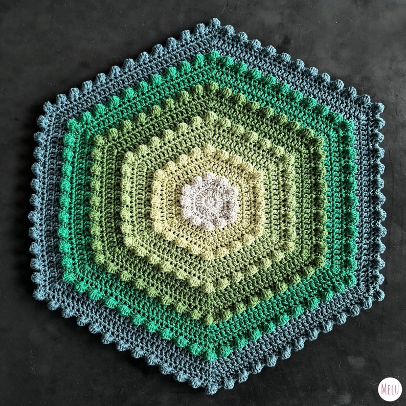 hexagon shaped crocheted bath mat in green tones, on a black background