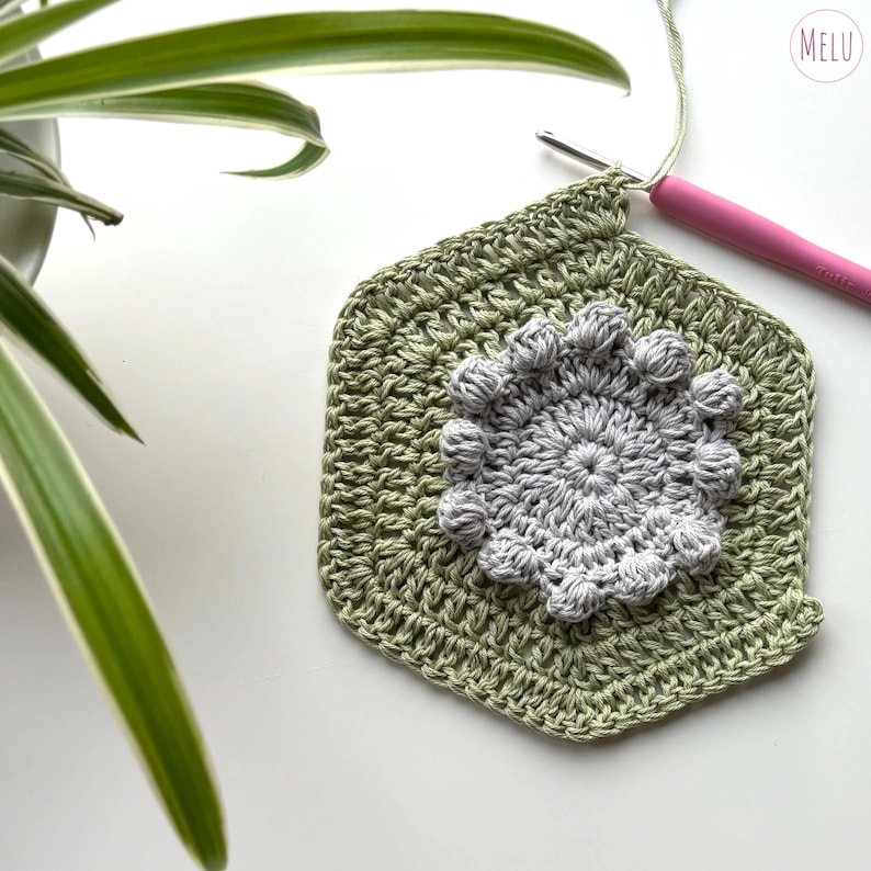 Crochet hook looped through cotton yarn, making a green and grey face cloth