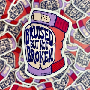 May include: A white sticker with a red, white, and purple illustration of a bandaged fist. The text "BRUISED BUT NOT BROKEN" is written in blue on the sticker.
