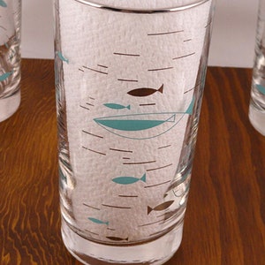 May include: Set of four clear glass drinking glasses with a silver rim. The glasses feature a mid-century modern design with brown and turquoise fish and lines.