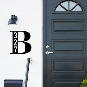 Peut inclure: Une plaque de numéro de maison noire et blanche avec le numéro 327 et la lettre B. La plaque est fixée à un mur blanc à côté d'une porte noire avec une fenêtre en verre.
