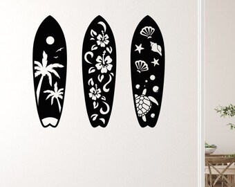 May include: Three black surfboards with white cut-out designs. One features a palm tree and sun, another has flowers, and the third displays seashells and a turtle. These decorative surfboards add a coastal theme to any room.