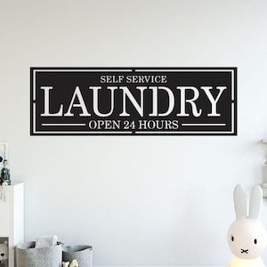 May include: Black and white sign with the text "Self Service Laundry Open 24 Hours" on a white wall.