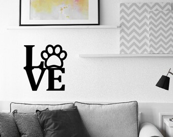 May include: Black and white wall art with the word "LOVE" and a paw print in the center of the "O". The art is displayed on a white wall above a gray couch.