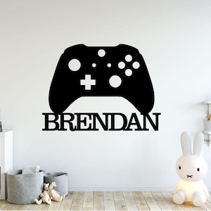 May include: Black and white vinyl decal of a video game controller with the name "BRENDAN" underneath. The decal is on a white wall.