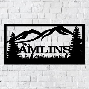 May include: Black metal sign featuring a mountain range silhouette, two pine trees, and the text "The Amlins" in a decorative font.