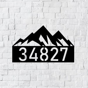 May include: Black metal house number sign with a mountain range design. The number 34827 is displayed in white.
