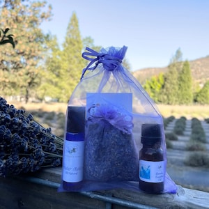 May include: A lavender-themed gift set in a purple mesh bag. The set includes a lavender essential oil bottle, a lavender roll-on bottle, and a small bag of dried lavender.