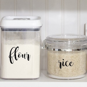 May include: Two clear plastic containers with labels on the front. The container on the left is labeled "flour" and the container on the right is labeled "rice".