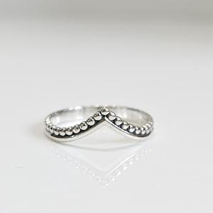 Może przedstawiać: Srebrny pierścionek z wzorem w kształcie litery V wykonanym z małych koralików.