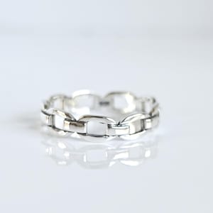 May include: A polished silver ring featuring a continuous chain link design. The band is composed of interconnected oval metal links with a smooth, reflective surface. A small hallmark is visible on the interior of the silver band.