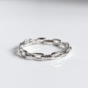 May include: A silver chain ring with a simple design. The ring is made of a series of connected oval links.