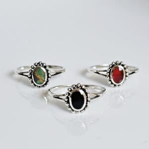 May include: Three silver rings with oval-shaped gemstones. The rings have a beaded design around the stone setting. The stones are green, red, and black.