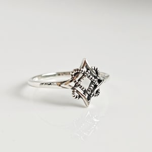 May include: A silver ring with a star-shaped design. The star is made of intertwined lines and has a black center.