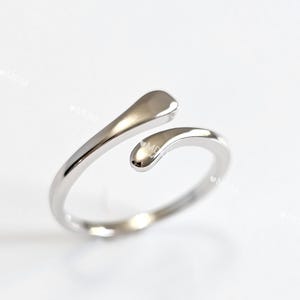 May include: A silver ring with a unique design featuring two curved, teardrop-shaped pieces.