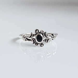 Op de afbeelding: Een zilveren ring met een zwarte ovale edelsteen in een bloemmotief.