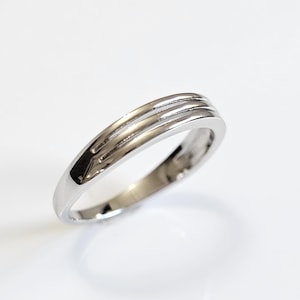 May include: A silver band ring with three parallel grooves around the band.