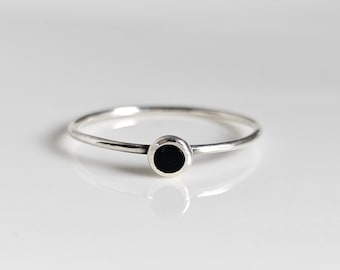 Peut inclure: Une bague en argent simple avec un petit cercle noir au centre.