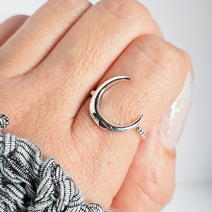 Può includere: Un anello d'argento a forma di mezzaluna con una fascia di perline. L'anello è indossato su un dito.
