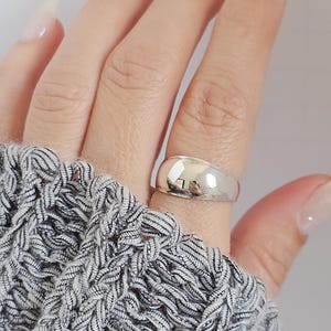 Peut inclure: Une bague en argent avec un dessus arrondi et bombé. La bague est portée à un doigt.