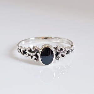 Peut inclure: Une bague en argent avec une pierre noire ovale sertie dans un délicat motif de filigrane.