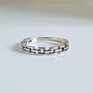 May include: A silver ring with a chain-like design. The ring is made of interlocking squares.