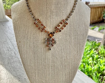 May include: A gold tone necklace with a teardrop-shaped pendant featuring clear and amber rhinestones.