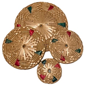 May include: A set of four round, woven baskets of varying sizes, constructed from light tan material with a radial pattern. Each basket features small, evenly spaced accents in alternating red and dark green colours woven into the circular design.