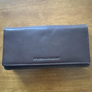 May include: A rectangular, dark brown leather wallet with the embossed text "SPIKES & SPARROW" centered on the front. The wallet is closed and appears to be empty, with a smooth, matte finish.