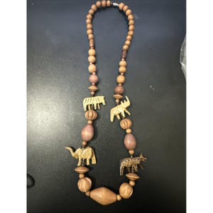 May include: A wooden beaded necklace featuring carved animal pendants. The necklace includes beads in various shapes and sizes, with animal figures such as elephants, rhinos, and other wildlife. The color palette is primarily natural wood tones.