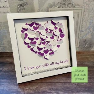May include: Framed artwork with a heart made of white and purple paper hearts. The text "I love you with all my heart" is below the heart. The white frame has a black border, and the artwork is embellished with small crystals.