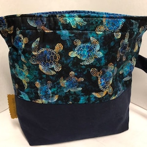 Könnte beinhalten: Eine blaue Kordeltasche mit einem dunkelblauen Boden. Die Tasche ist aus Stoff mit einem Muster von Meeresschildkröten auf dunkelblauem Hintergrund. Die Tasche hat zwei blaue Kordeln.