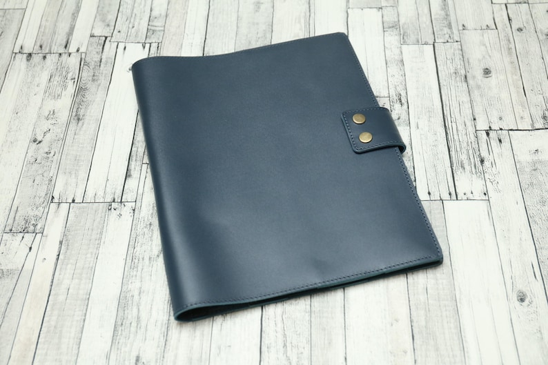 May include: A dark blue leather folder with two brass snaps on the front flap.