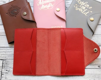 May include: A red leather passport holder with three interior pockets and a flap closure. The holder is open and the interior is visible. The holder is made of high-quality leather and has a classic design.