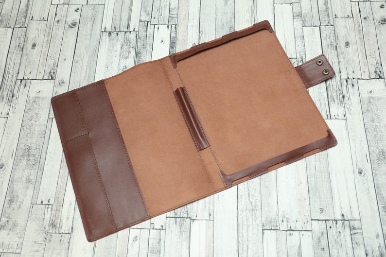 May include: A brown leather folder with a flap closure and a pen holder. The folder is open and the inside is lined with a light brown fabric.