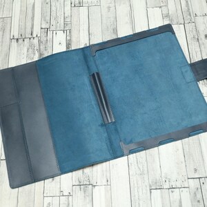 May include: A blue leather notebook with a flap closure and a pen holder. The notebook is open to reveal a blue interior.